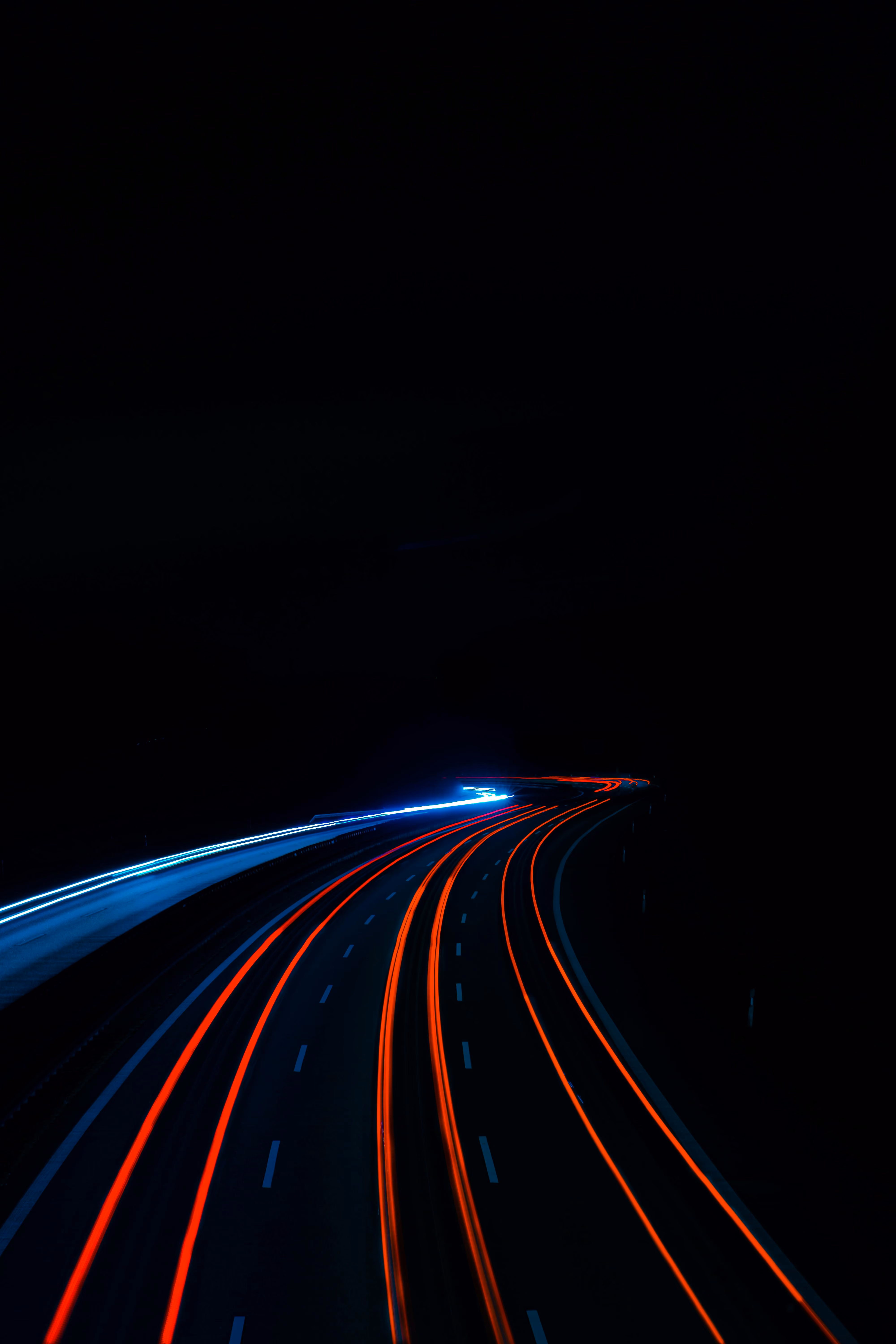 Lichtspuren von Fahrzeugen auf einer mehrspurigen Autobahn bei Nacht, rote Rücklichter und weiße Scheinwerfer.