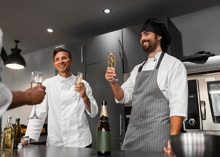 Chefs celebrating in a modern kitchen with champagne, smiling and toasting with glasses.