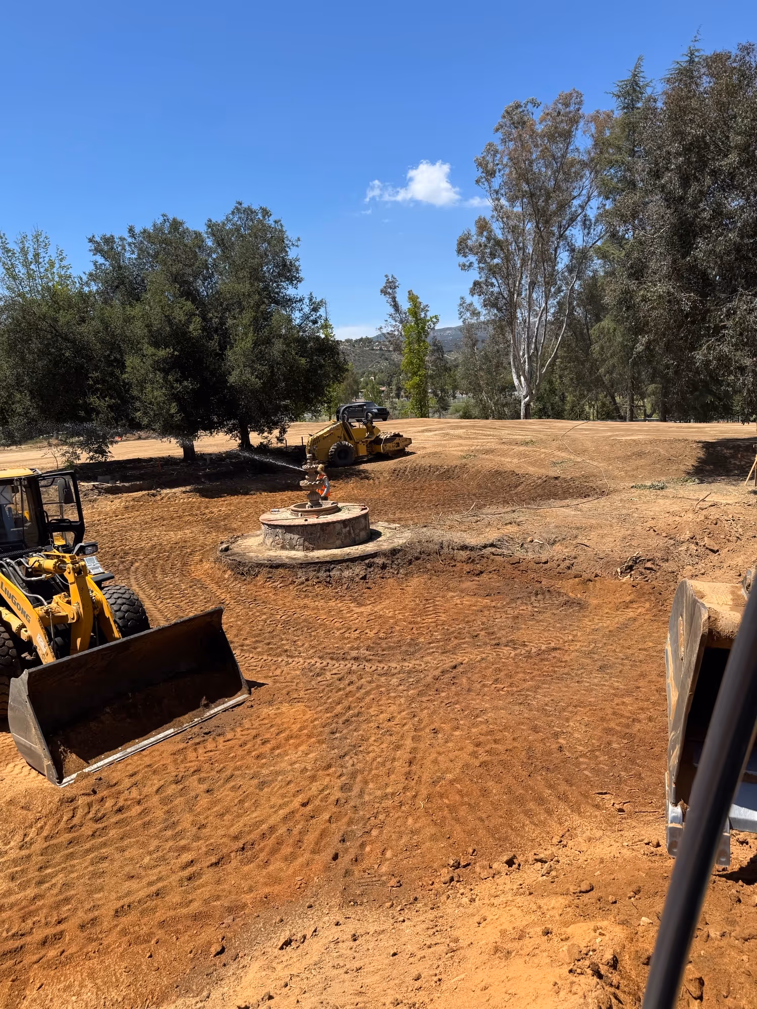 Construction site with grading equipment and concrete utility structure surrounded by dirt work.