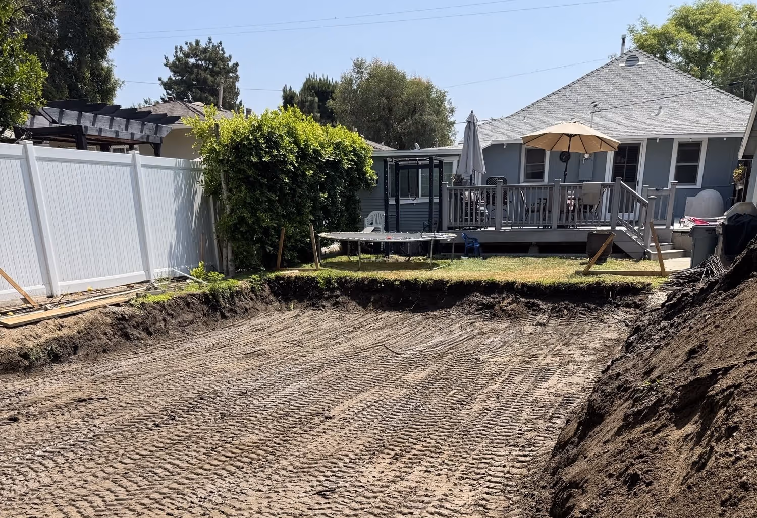 Excavated residential backyard with rebar foundation prep and concrete forms near existing home.