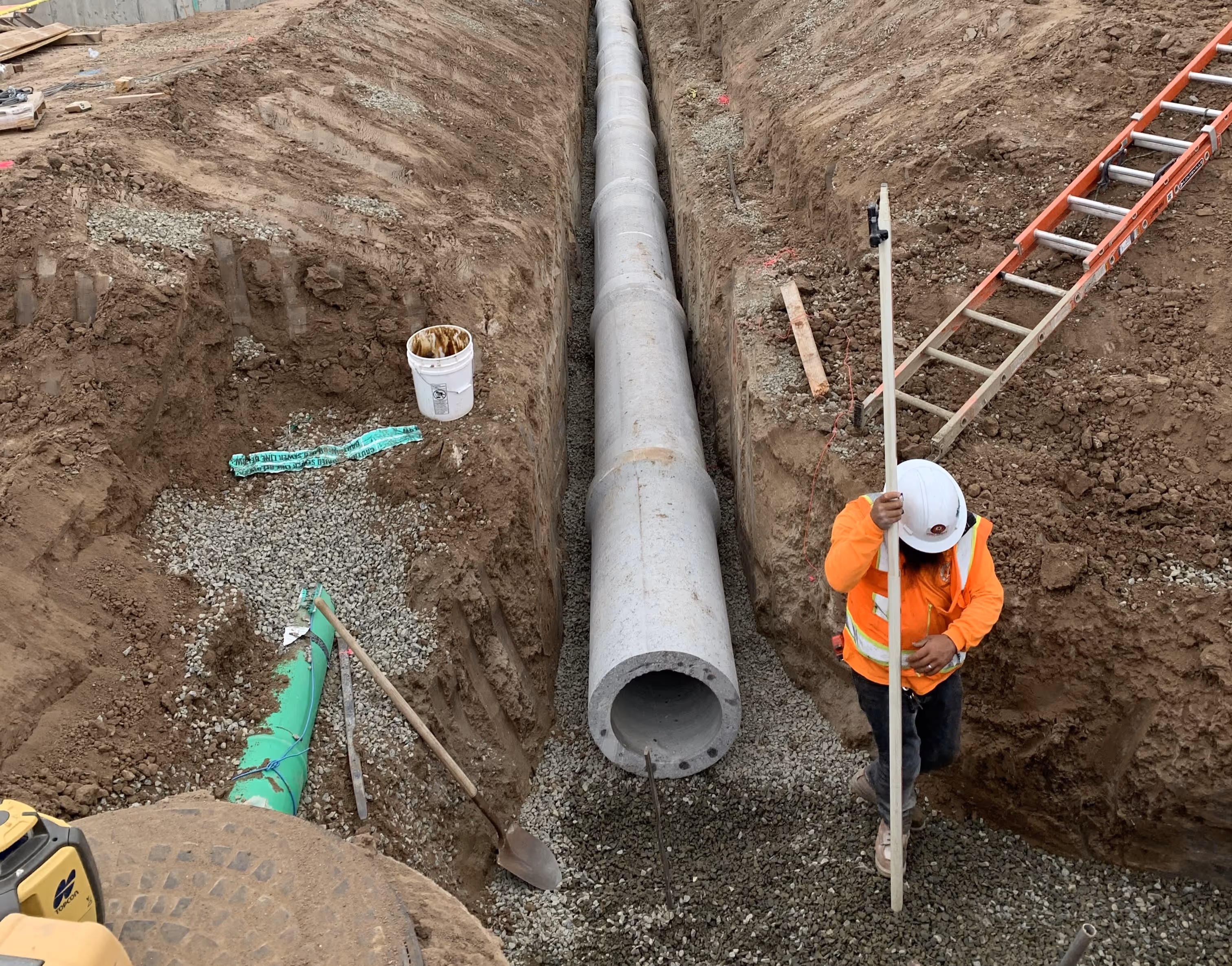 Worker inspecting alignment of stormwater or sewer pipeline during trench excavation.