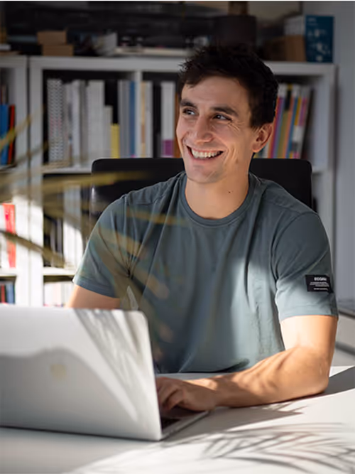 Smiling person working on laptop in home office with bookshelves behind