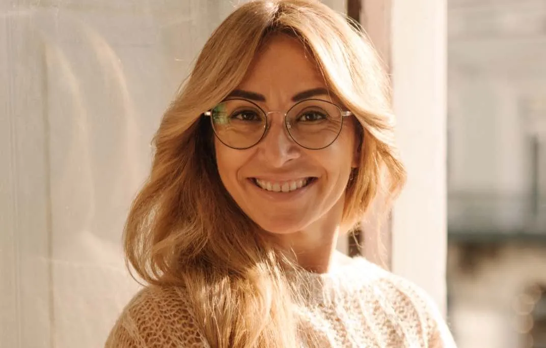 Eine blonde Frau in einem Strickpullover trägt eine Gleitsichtbrille und lächelt.