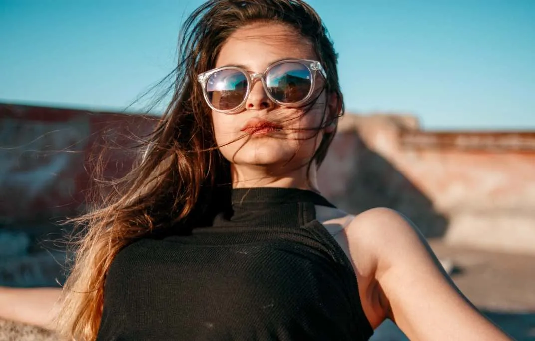 Eine modische junge Frau trägt eine moderne Sonnenbrille während ihre Haare im Wind wehen.