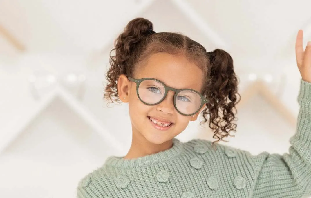 Ein lächelndes Kind in fröhlicher Atmosphäre trägt eine Brille extra für Kinder.