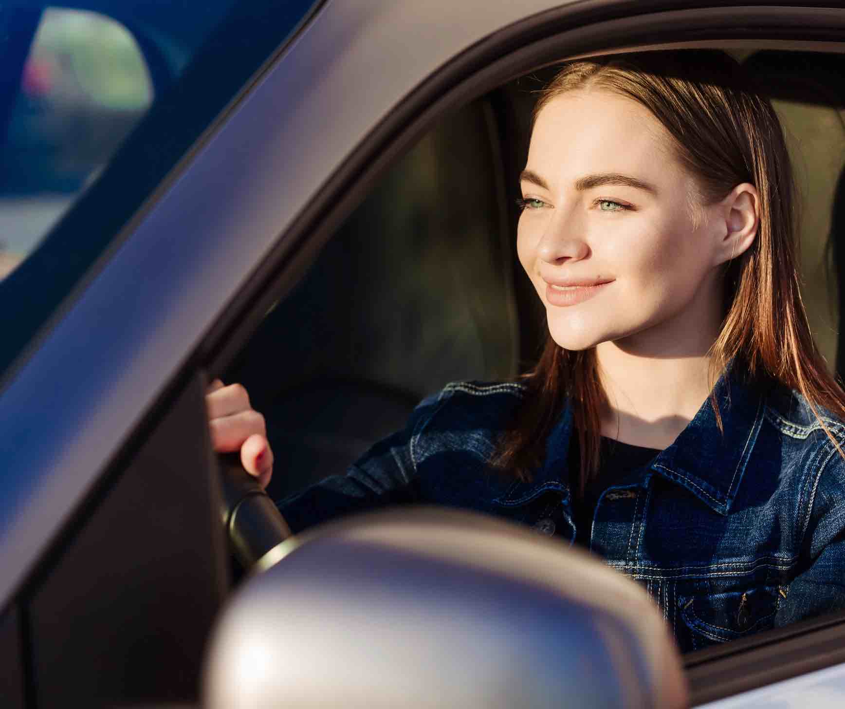 Ein junges Mädchen sitzt glücklich in ihrem ersten Auto nach der Fahrprüfung für die sie einen  Führerscheinsehtest bei Optik Hess absolviert hat.