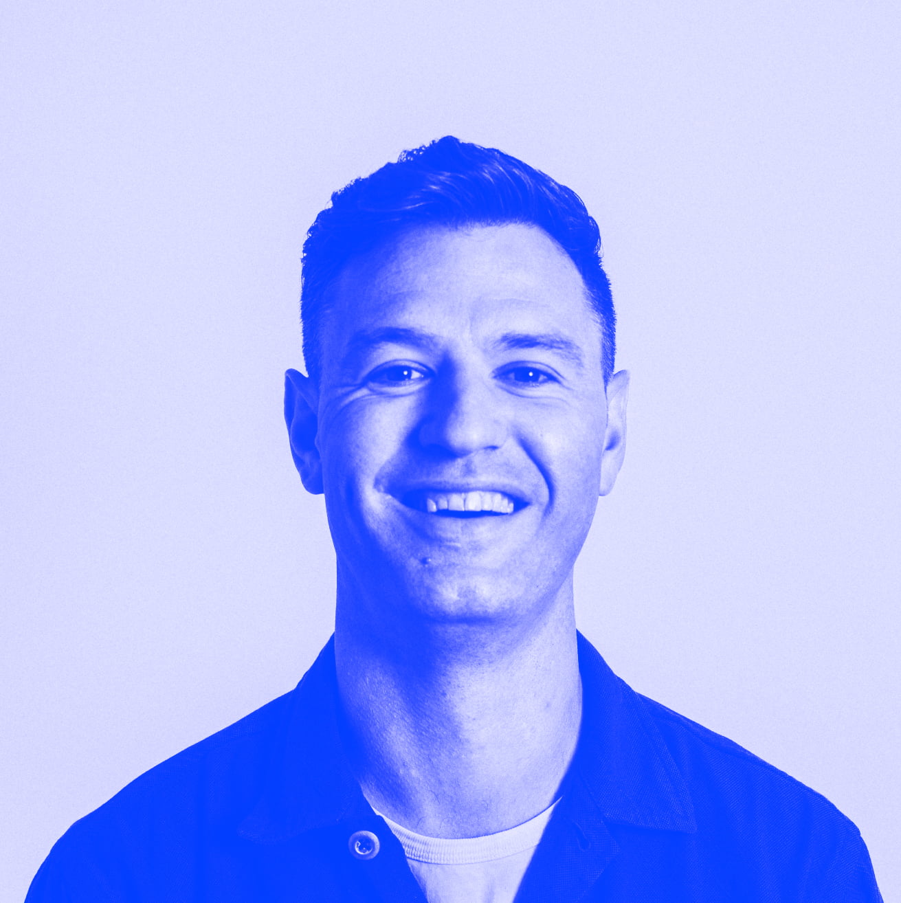 An image of a man with dark hair, wearing a jacket and white T-shirt leaning backwards and smiling at the camera. Blue filter on the image. 