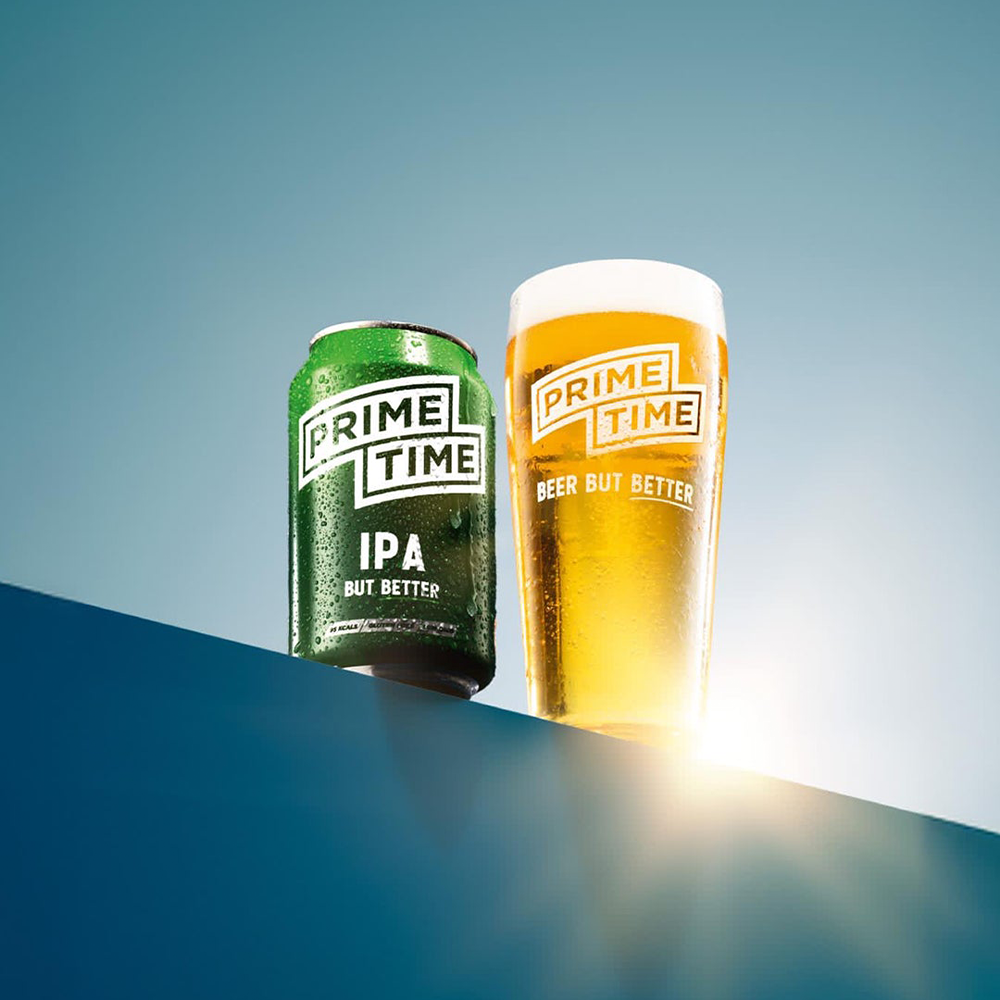 A Prime Time green can and pint of beer on an angled shelf, with a blue background.
