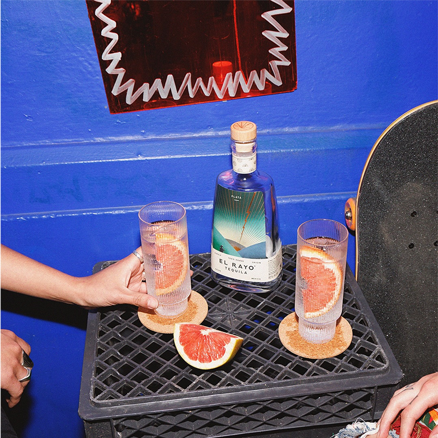 Two glasses of Tequila and soda with grapefruit slices on a side table against a cobalt blue wall.