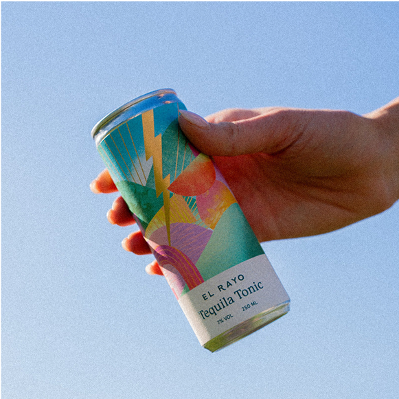 Hand holding a colourful drinks can with the sky in the background.