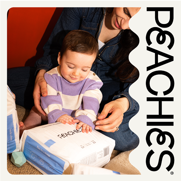 A young child wearing a stripey purple jumper holding a Peachies nappy package. 