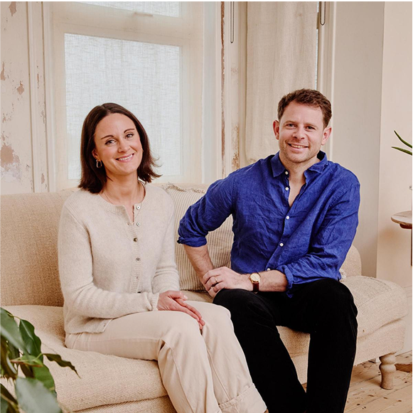 Naked Paper Founders: A man in a blue shirt sitting next to a woman with brown hair and white cardigan on a beige sofa. 
