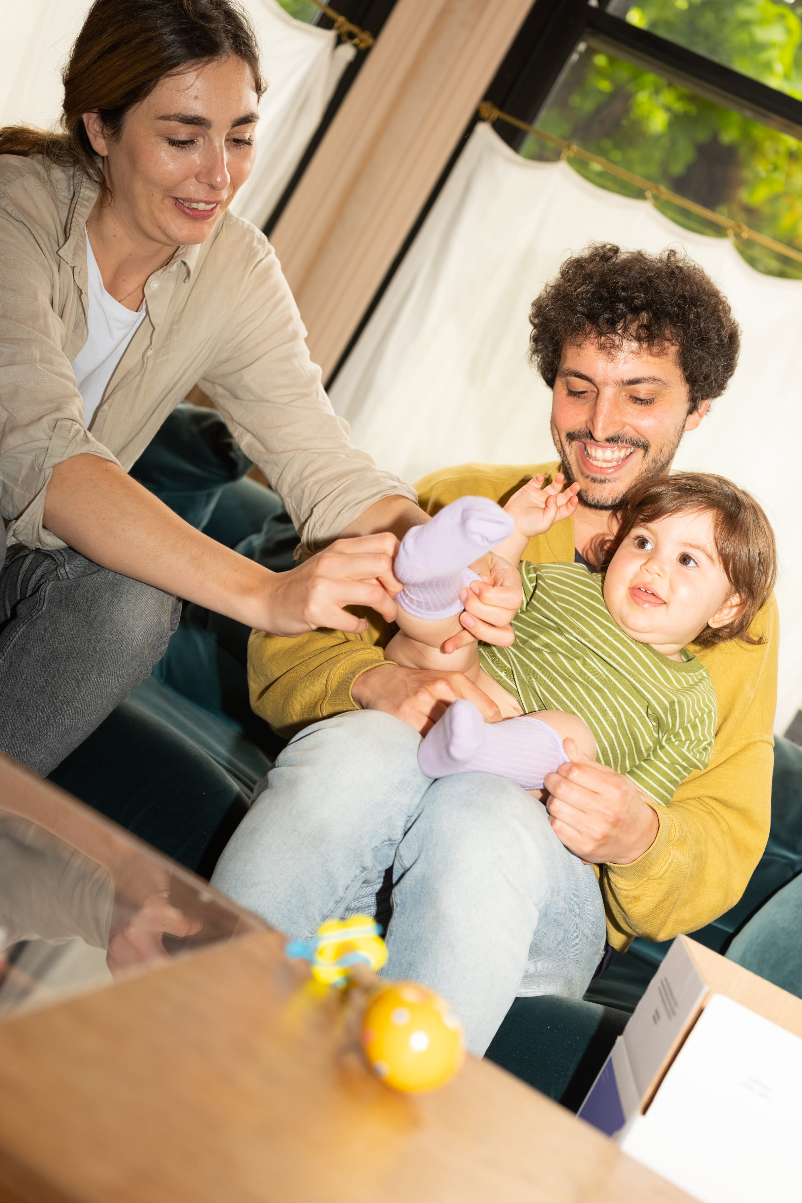 A toddler being held by a young man while a woman attempts to put a purple sock onto the toddler. All smiling. 