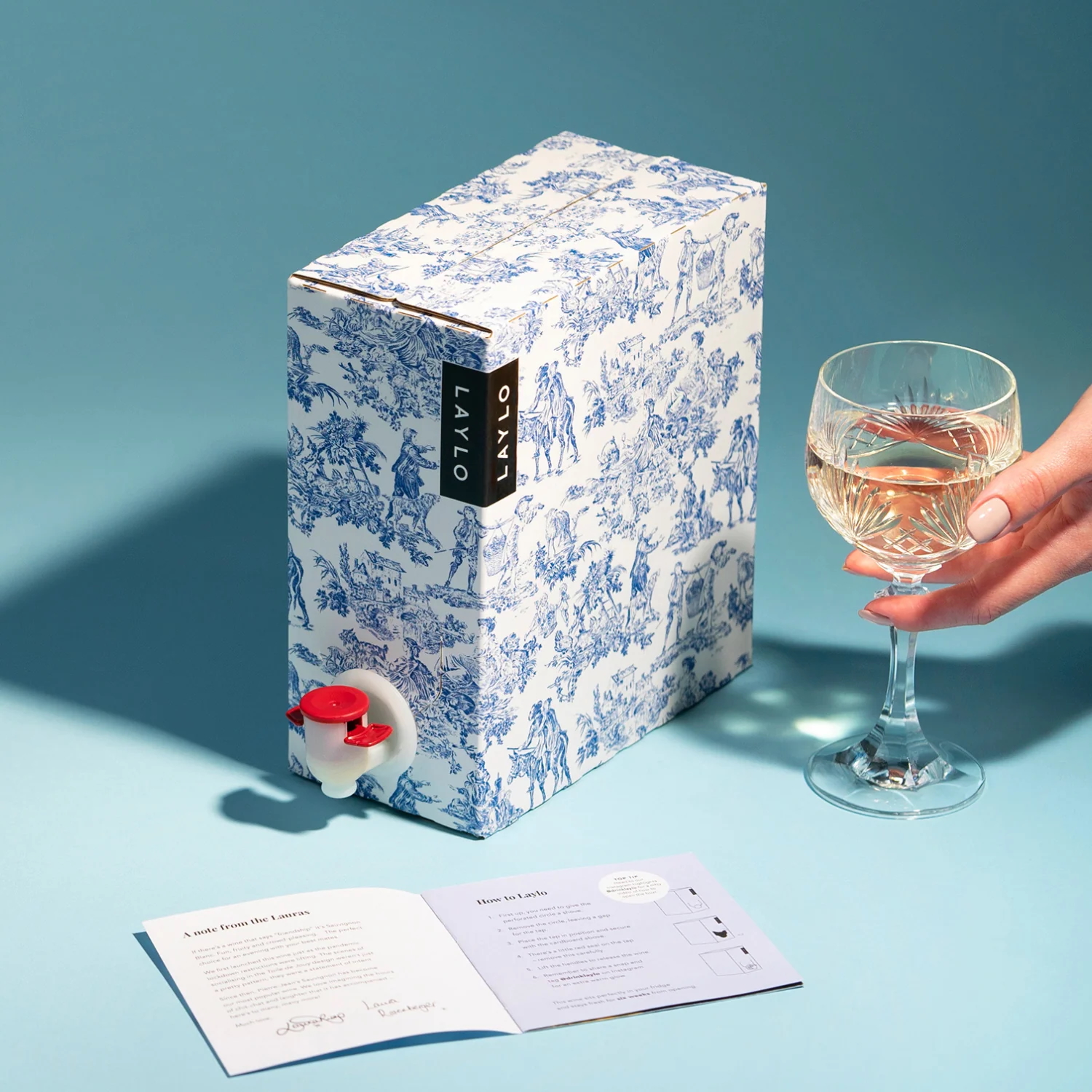 Blue background, boxed wine and wine glass in someone's hand. 