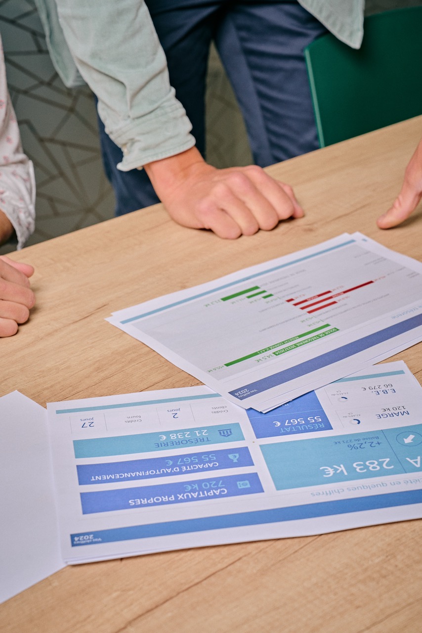 Deux personnes discutant autour d'une table en bois avec des documents financiers imprimés posés dessus.