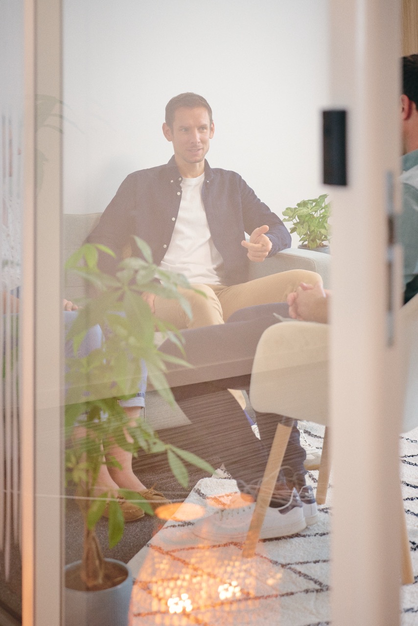 Un homme parlant en réunion assis sur un fauteuil dans un bureau moderne avec des plantes visibles.