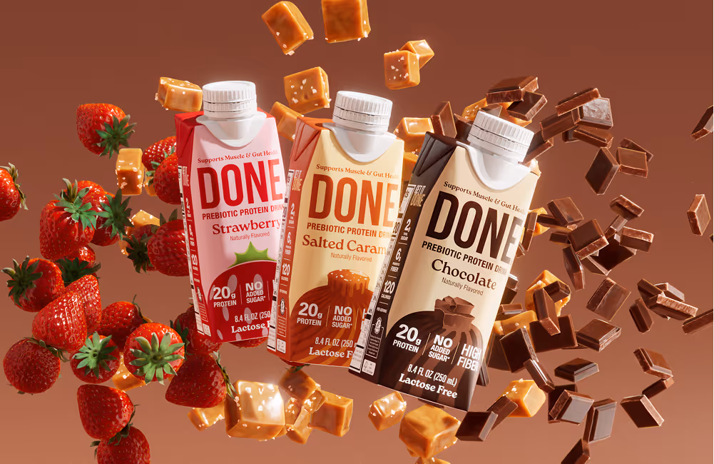DONE Drinks Strawberry, Salted Caramel, and Chocolate protein beverages floating with fresh strawberries, caramel chunks, and chocolate pieces on a warm-toned background.