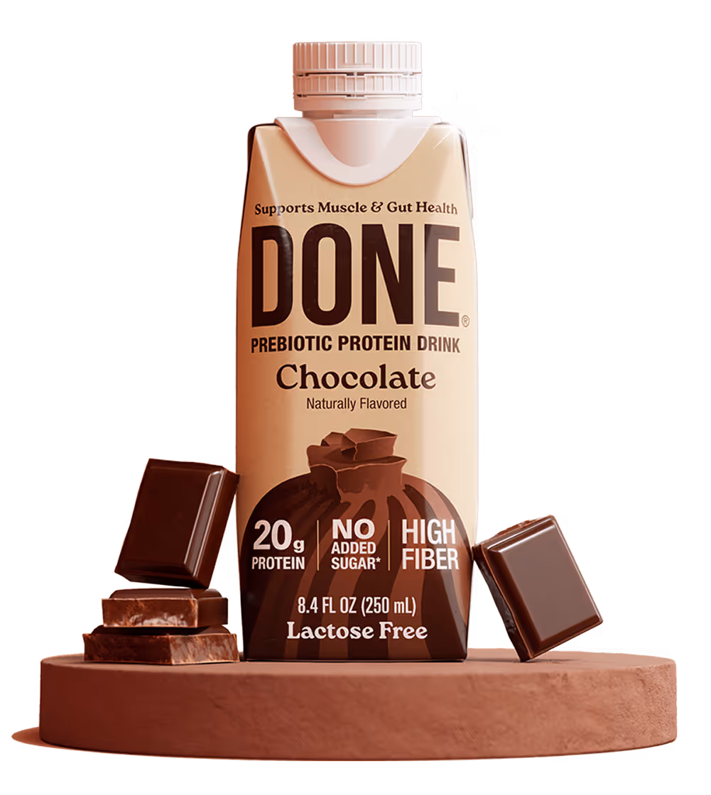 DONE Drinks Chocolate protein shake standing on a round brown pedestal with chocolate chunks.