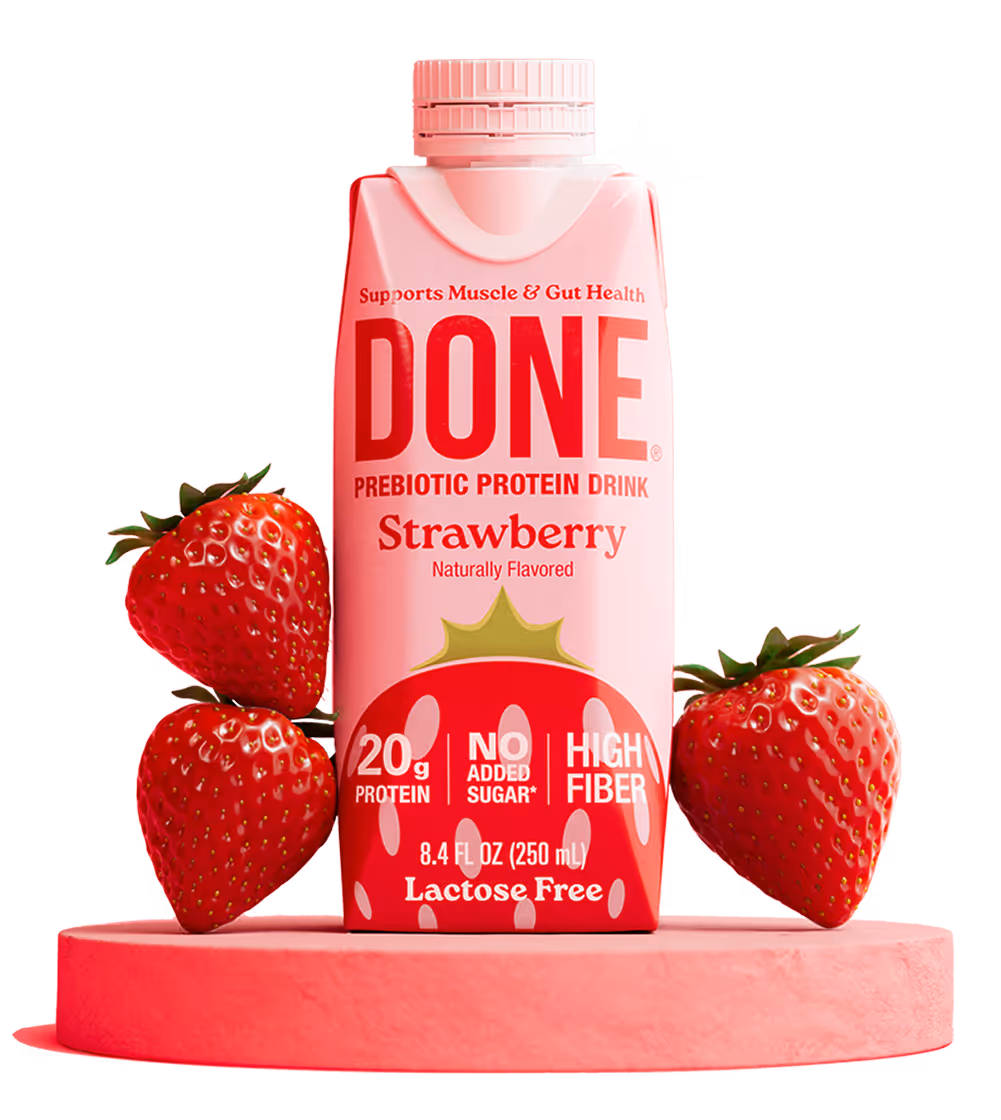 DONE Drinks Strawberry protein shake displayed on a pink pedestal with fresh strawberries.