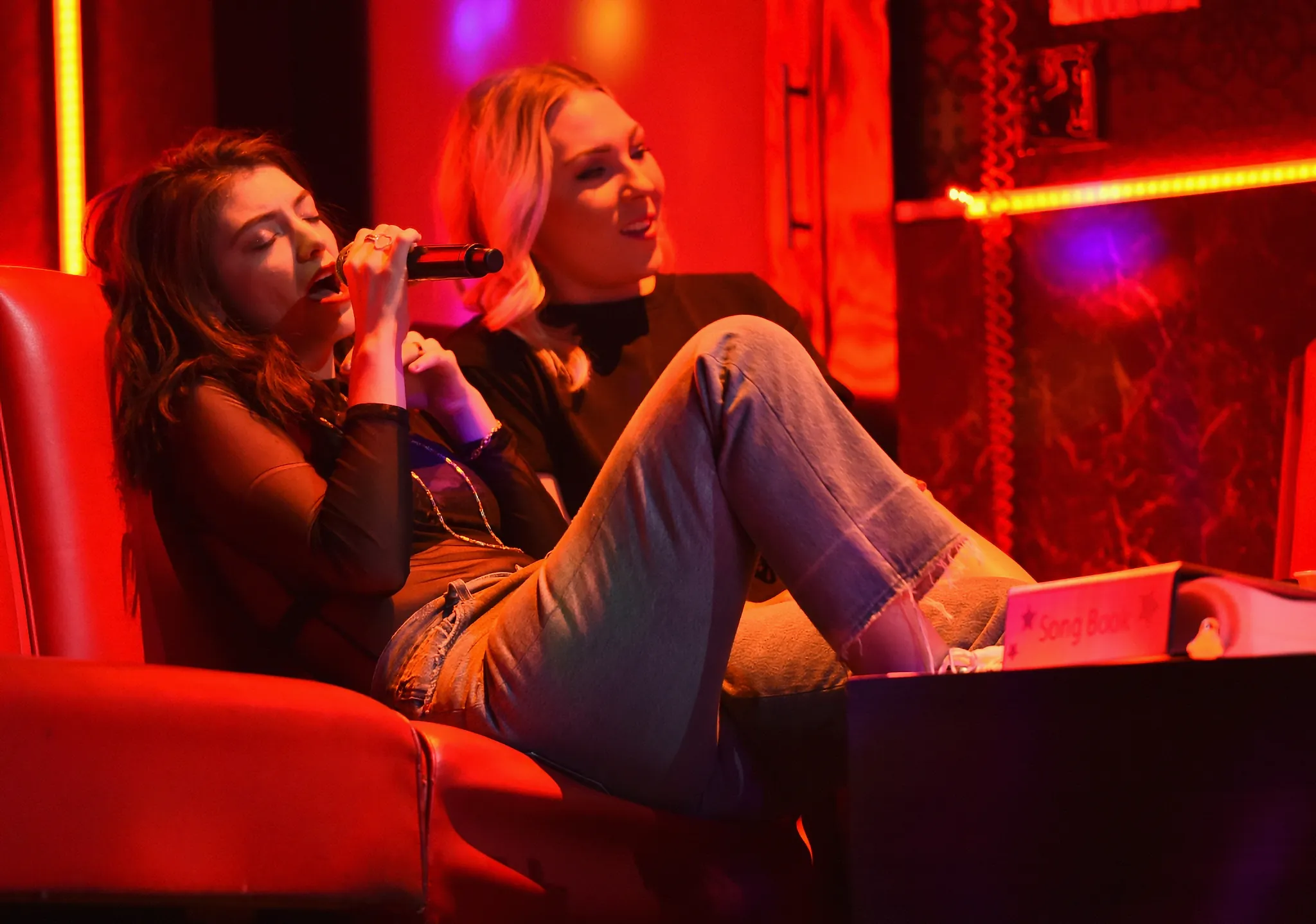 Lorde sitting on a sofa singing in a Karaoke room