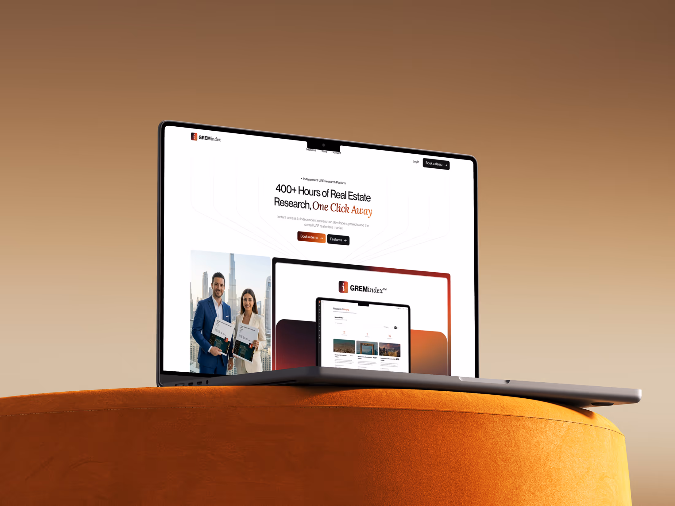Laptop on orange cushion showing GREMindex website with real estate research content and photos.
