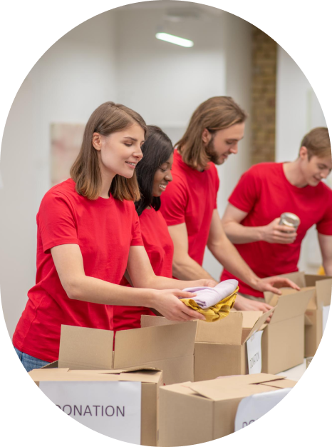 Four people in red shirts pack items into donation boxes on a table.