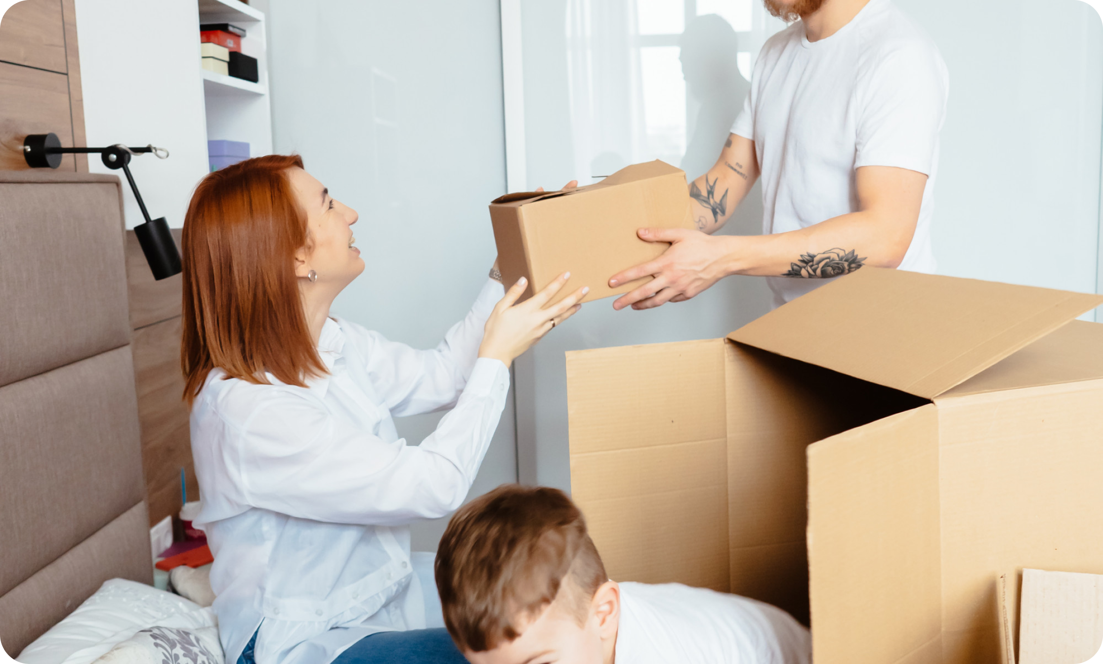 Man and woman unpacking boxes with their child inside a cosy bedroom after a successful move with IMG Removals in Birmingham—family-focused, relaxed, and settling into their new home.