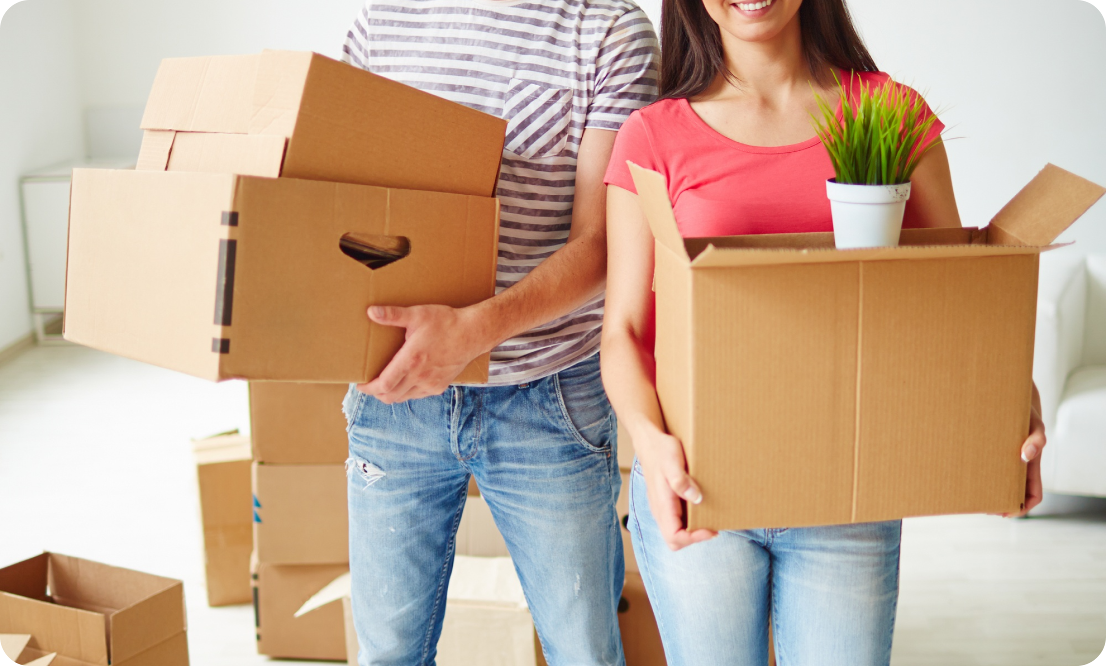 Young couple standing together and smiling while holding packed boxes in their new home—ready to unpack and settle in after a smooth move with IMG Removals in Birmingham.