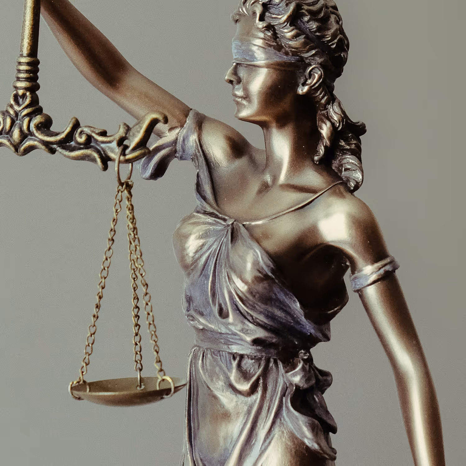 Close-up of a bronze Lady Justice statue holding balanced scales and wearing a blindfold.