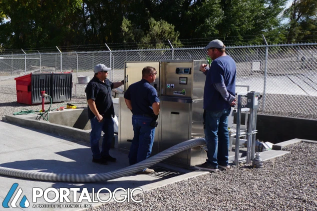 Three men surrounding a septage receiving station keypad.