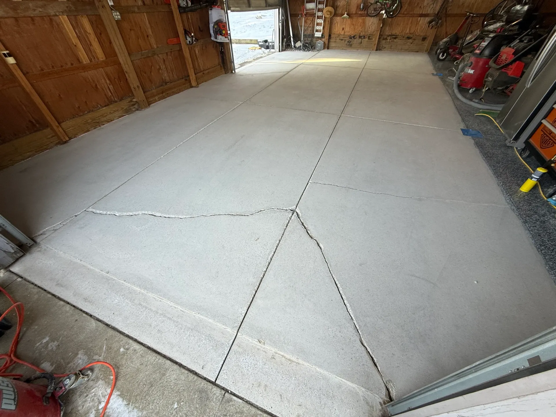Garage concrete slab with visible cracks and taped layout lines before floor repair and coating.
