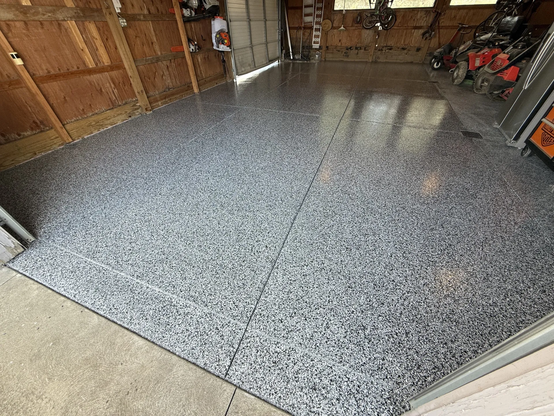 Finished garage with gray-and-black domino flake polyaspartic floor coating, glossy non-porous finish, and clean control joints.
