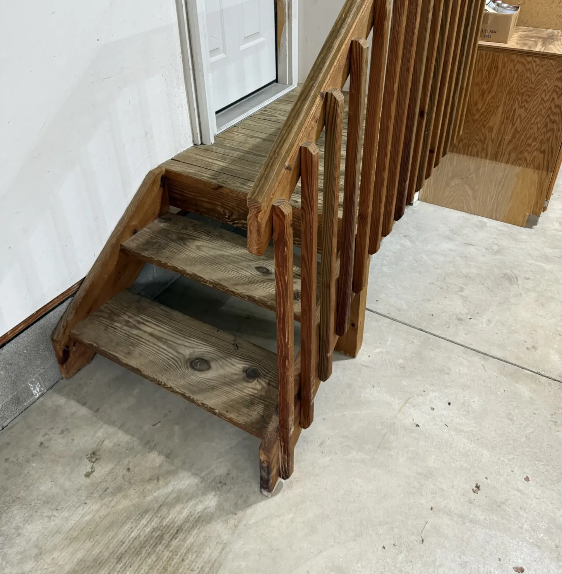 Garage steps and railing before coating, with unfinished concrete and wood railing.