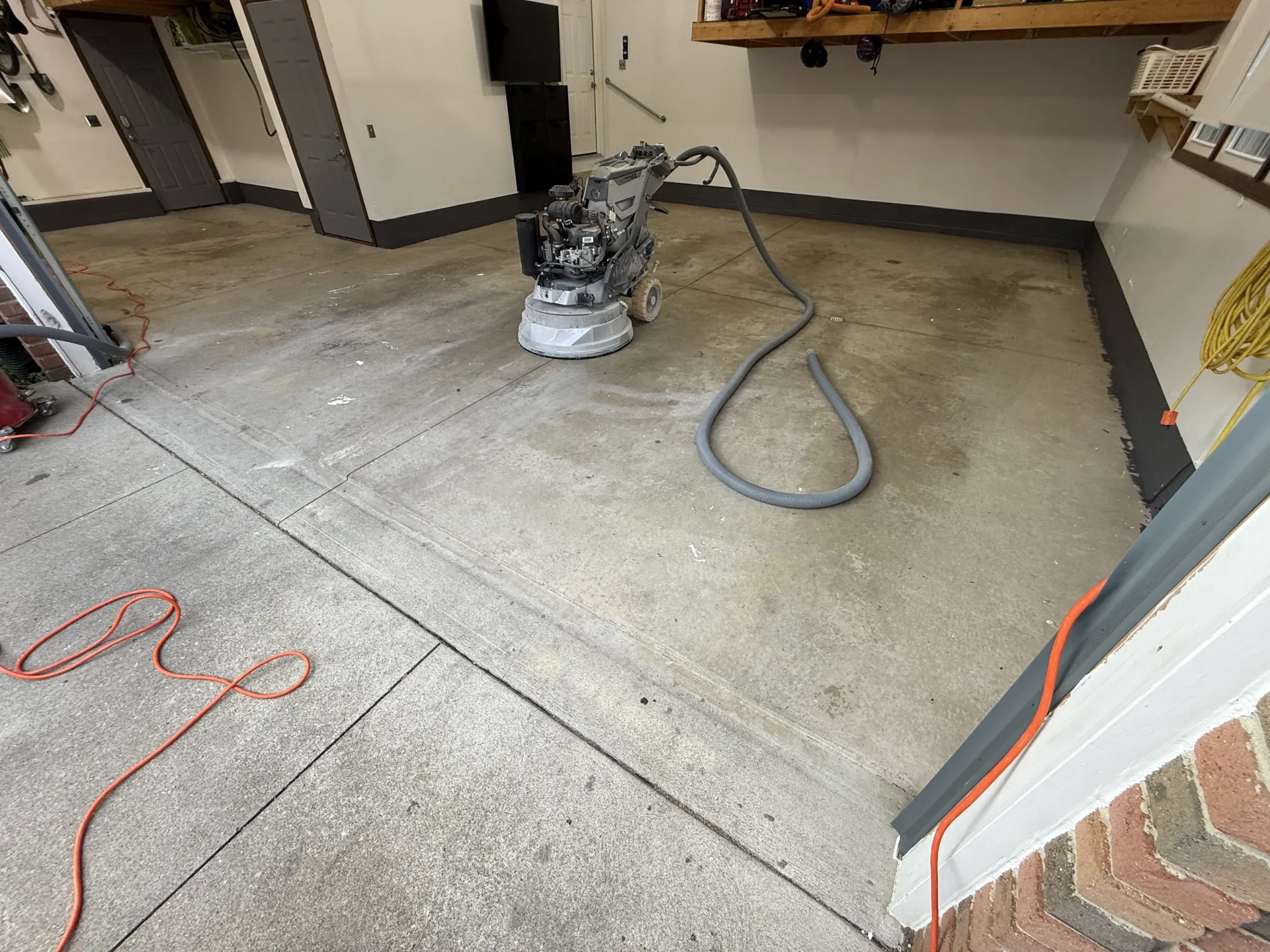 Garage concrete floor before coating, with grinder and prep equipment on the slab.