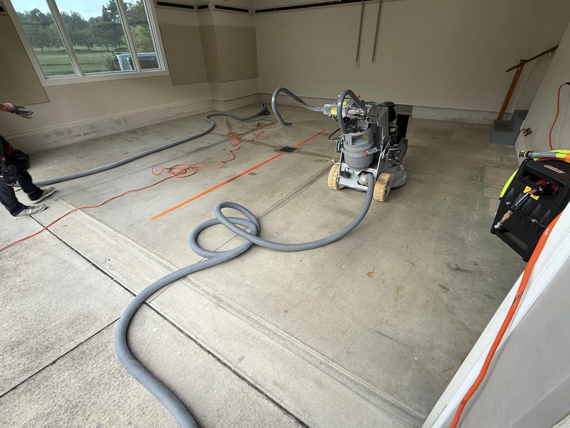 Garage concrete floor during surface prep with grinding equipment and vacuum hose.