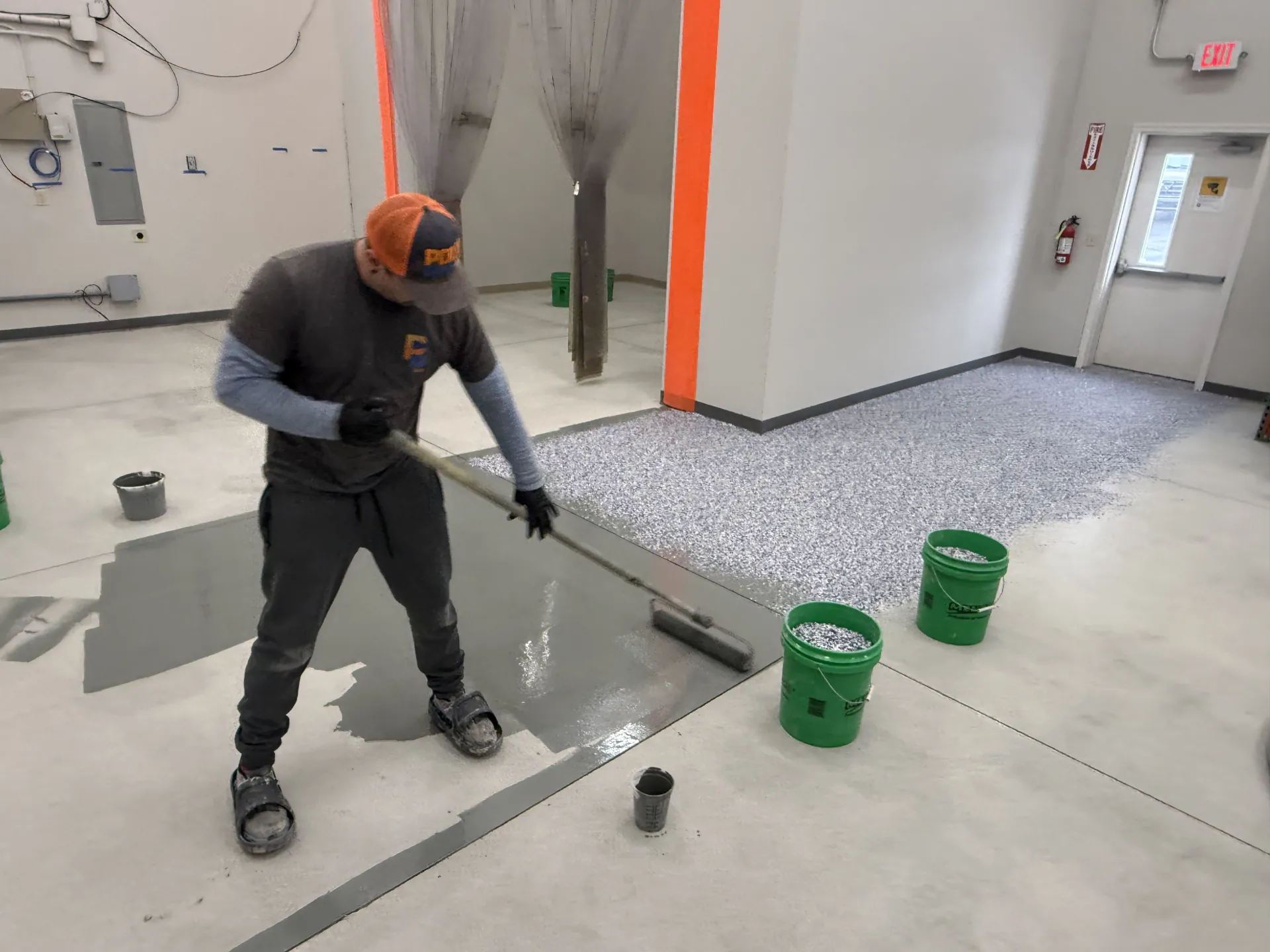 Poly Guys technician applying the polyurea base coat during installation of a custom polyaspartic flake floor system at Keller Construction's warehouse facility.
