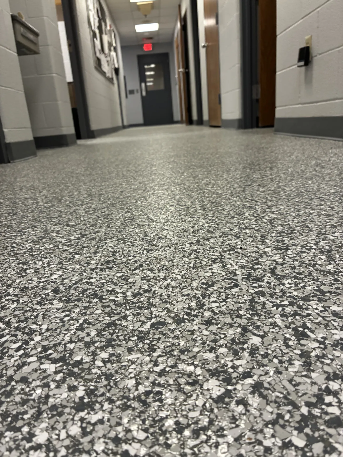 Close-up view of a completed polyaspartic flake floor coating in a commercial hallway, showcasing a durable gray, white, and black flake blend with a seamless, slip-resistant finish.
