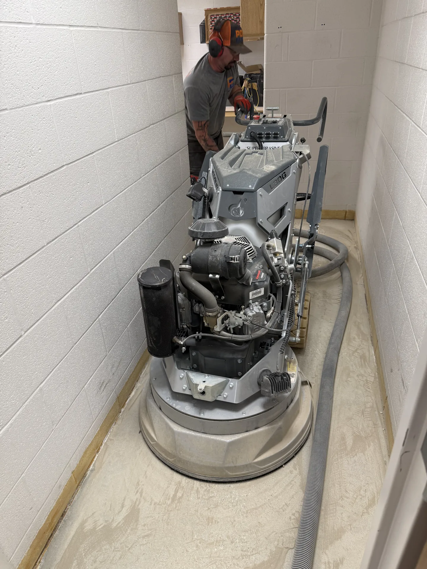 Poly Guys technician diamond grinding a narrow hallway floor during concrete surface preparation before installation of a commercial polyaspartic flake coating system.