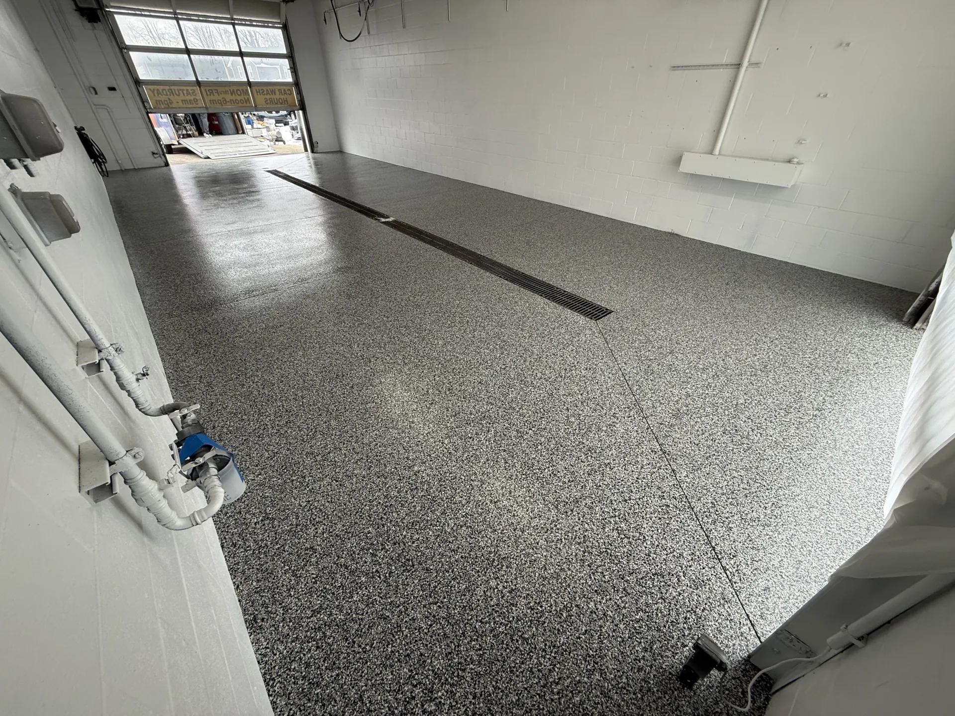 Completed polyaspartic flake floor coating in a commercial wash bay, featuring a seamless gray flake blend and integrated trench drain for easy cleaning and drainage.