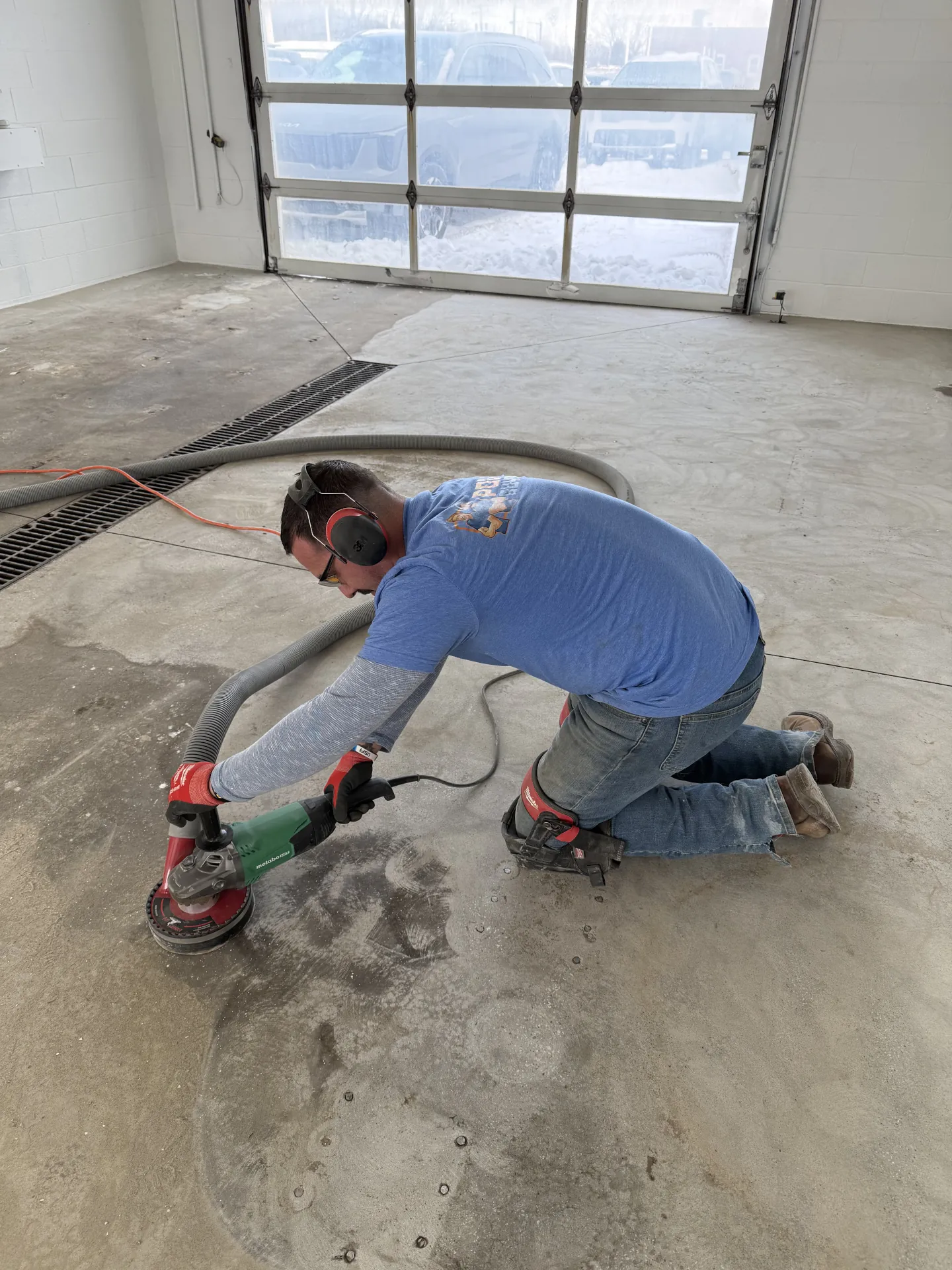 Poly Guys technician grinding concrete edges and detailed areas during surface preparation for a commercial polyaspartic floor coating installation.