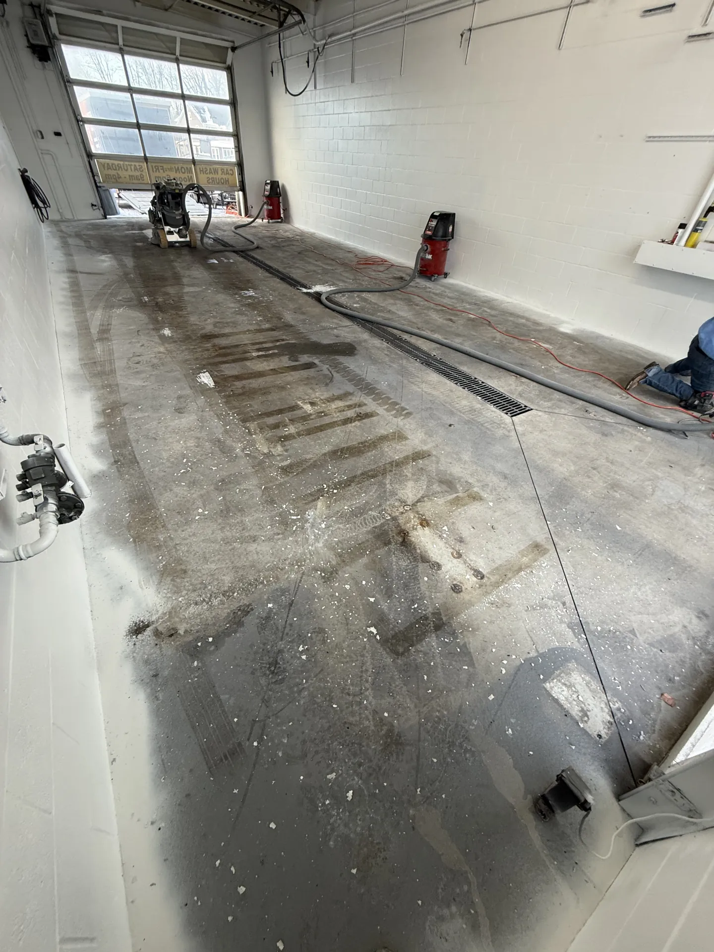 Commercial wash bay concrete floor before coating installation, showing existing surface conditions and preparation work underway prior to a polyaspartic flake floor system.