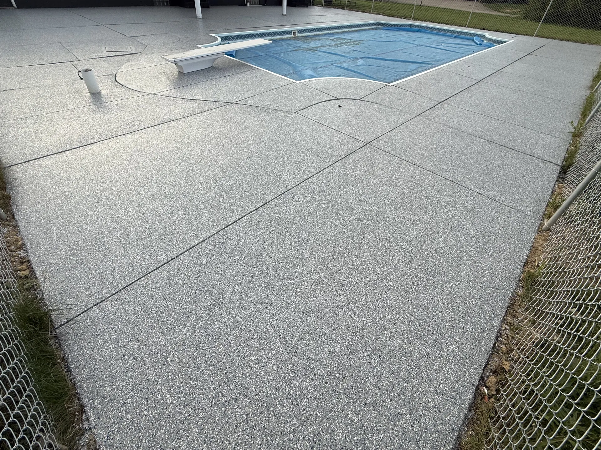 Completed polyaspartic flake pool deck coating featuring a light gray decorative flake blend, creating a seamless, slip-resistant surface around an in-ground swimming pool.