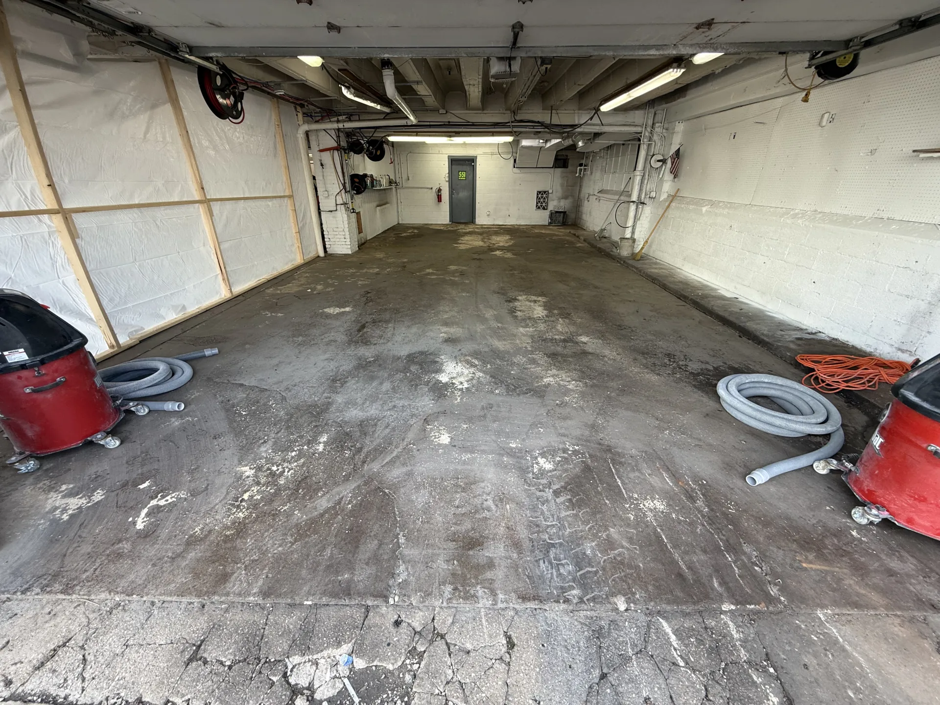 Commercial garage bay concrete floor before restoration and coating installation, showing worn concrete, surface contamination, and preparation equipment staged for the project.