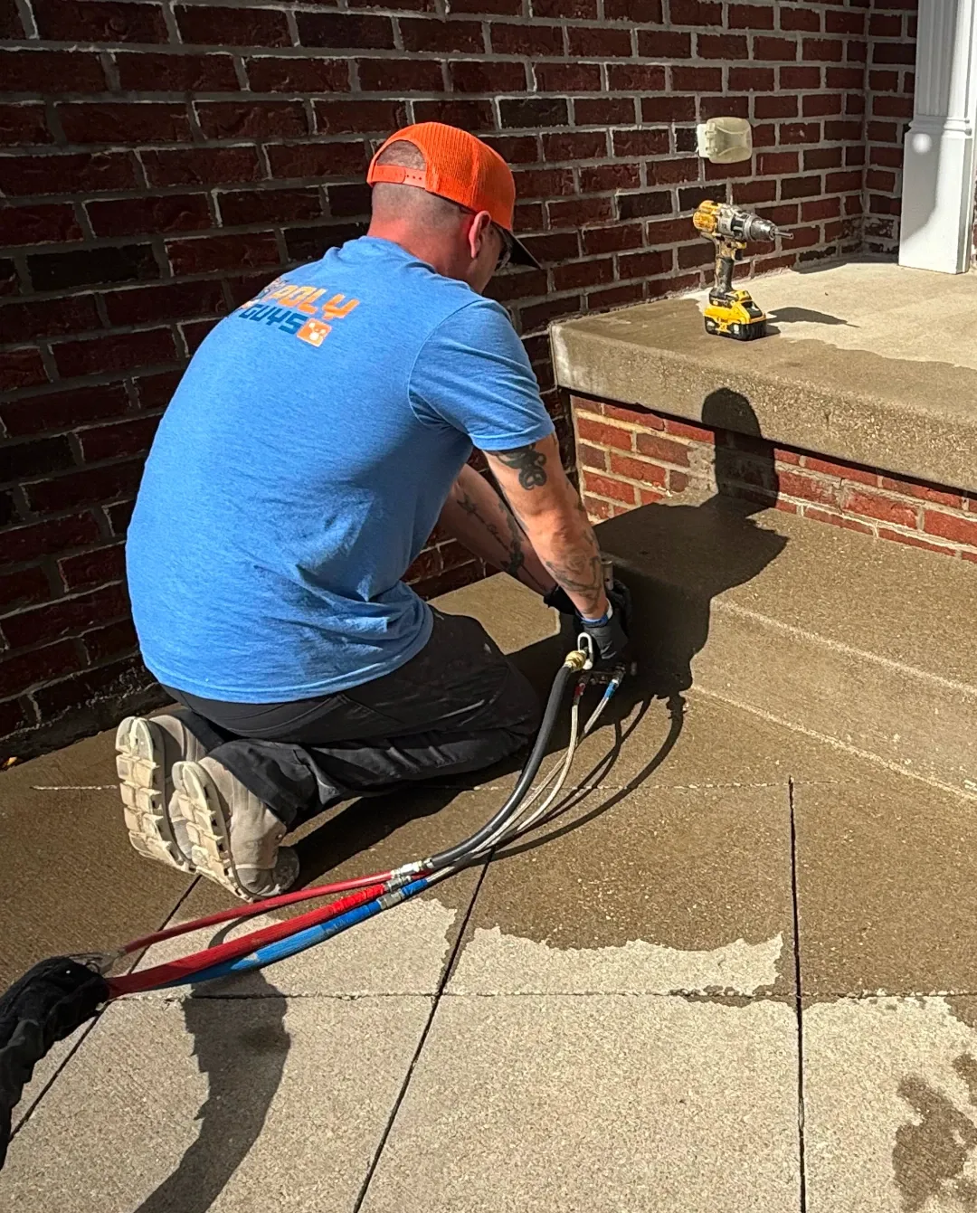 man in blue shirt and orange hat injecting foam into a concrete patio to lift it