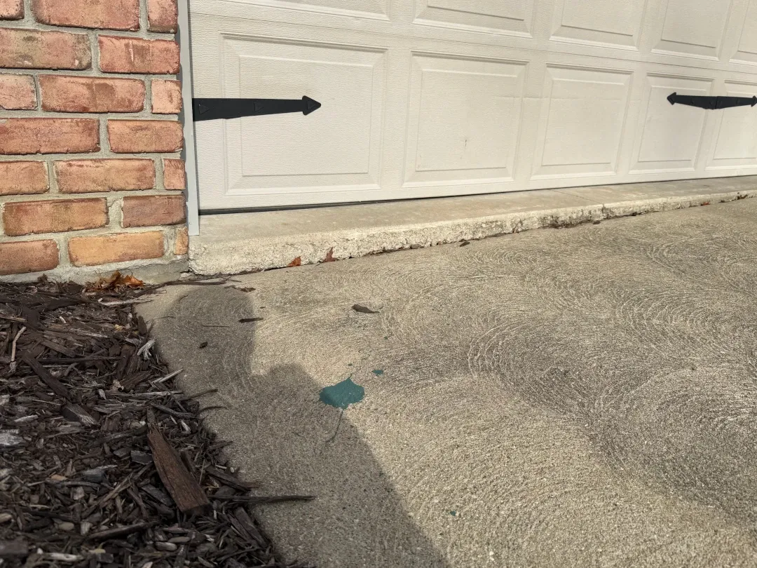 Sunken driveway in front of a garage with visible settlement causing an uneven transition between the driveway and garage slab.