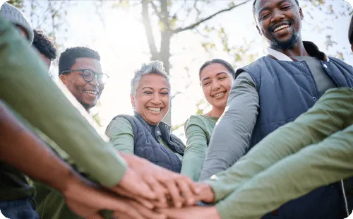 Diverse team standing together outdoors with hands stacked in the center, showing teamwork and collaboration