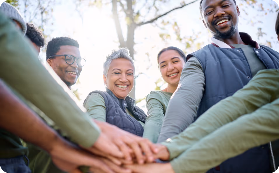 Diverse team standing together outdoors with hands stacked in the center, showing teamwork and collaboration