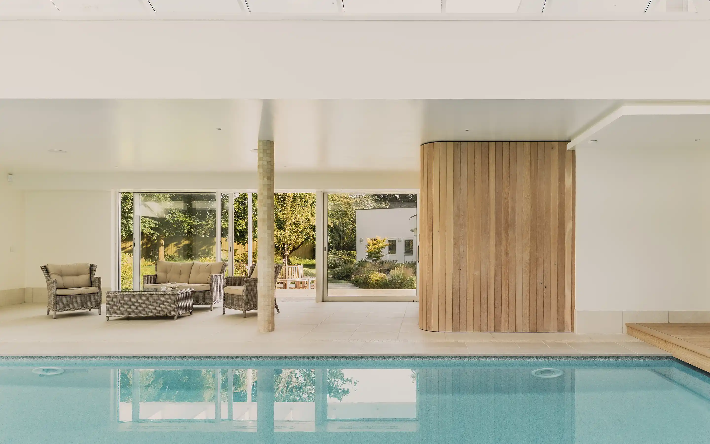 Close-up view of a swimming pool corner with turquoise water, light brown poolside tiles, and speckled stone, with shadows cast across the surface.