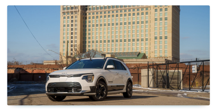 A silver remote-controlled sharing car in front of a large building in Detroit on a sunny winter day