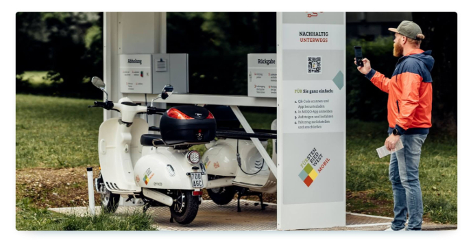 A man stands in front of a sharing scooter in its station and scans the QR code